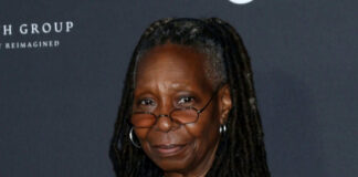 A smiling woman with dreadlocks wearing glasses at a red carpet event
