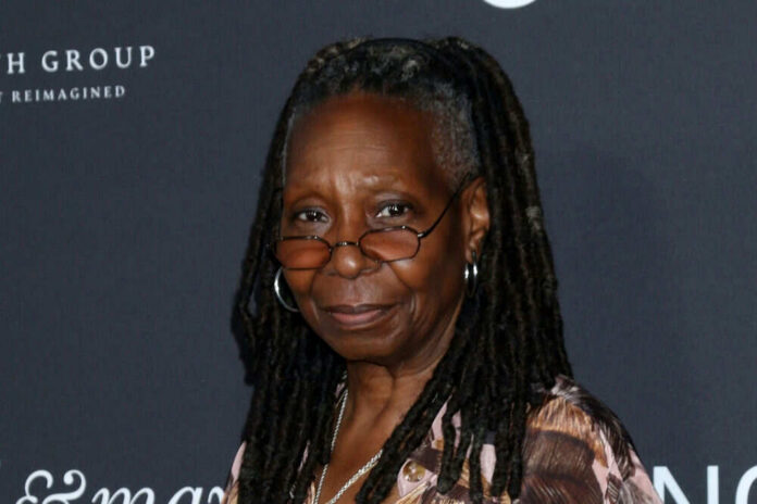 A smiling woman with dreadlocks wearing glasses at a red carpet event