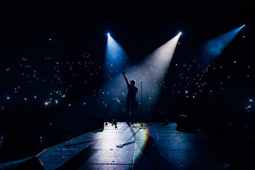 Silhouette of a musician performing on stage with bright lights and an engaged audience