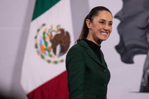 A woman in a green suit smiling in front of the Mexican flag