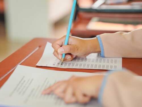 A student's hand holding a pencil while writing on a sheet of paper