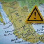 Cartel Chaos Traps US Tourists A yellow warning sign placed on a map of Mexico