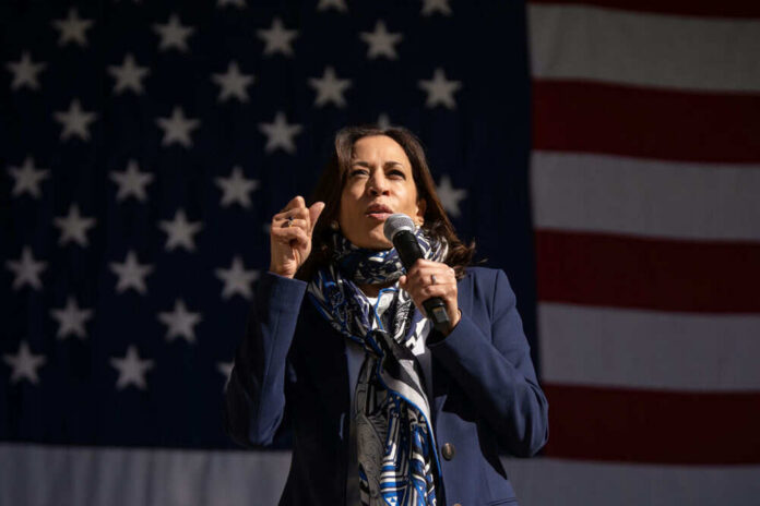 Person speaking into microphone in front of U.S. flag.