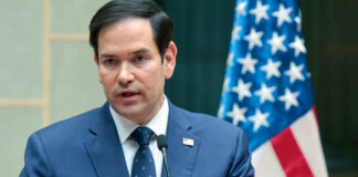 Man in suit speaking at podium with flag behind