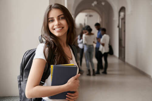 Smiling student holding books in a school hallway