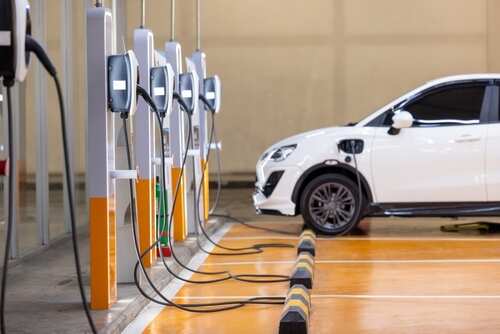 A white electric vehicle parked at a charging station with multiple chargers
