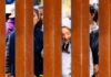 Individuals standing behind a border wall, expressing various emotions