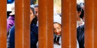 Individuals standing behind a border wall, expressing various emotions
