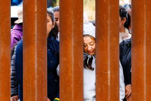 Individuals standing behind a border wall, expressing various emotions