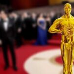 Golden Oscar statue in the foreground with blurred celebrities in formal attire in the background