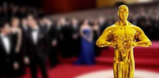 Golden Oscar statue in the foreground with blurred celebrities in formal attire in the background