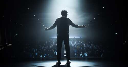 Silhouette of a speaker on stage with an audience in the background