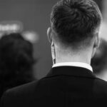 Taxpayers Hit With Harris’s Protection Bill? Back view of a man in a suit with an earpiece, surrounded by other individuals