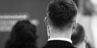 Back view of a man in a suit with an earpiece, surrounded by other individuals