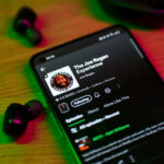 Phone screen showing a podcast with earbuds nearby