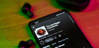 Phone screen showing a podcast with earbuds nearby
