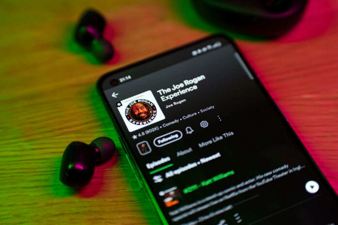 Phone screen showing a podcast with earbuds nearby