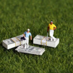 Two miniature golfers standing on stacks of money on grass