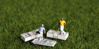 Two miniature golfers standing on stacks of money on grass