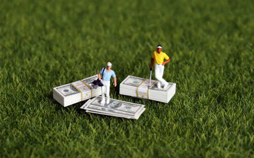 Two miniature golfers standing on stacks of money on grass