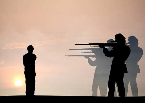 Silhouette of a person standing before soldiers aiming rifles at sunset
