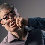 A man with glasses appears to be punched in the face by another person's fist
