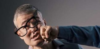 A man with glasses appears to be punched in the face by another person's fist