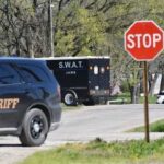 A sheriff's vehicle and a SWAT truck near a stop sign on a road