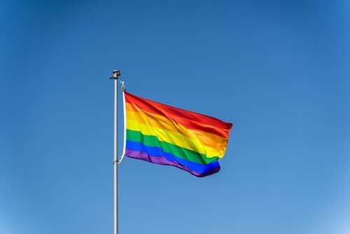 Rainbow flag waving against a clear blue sky