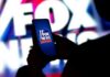 Fox News Feud: Trump Demands Co-Host’s Removal A person holding a smartphone displaying the Fox News logo against a colorful background