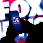 A person holding a smartphone displaying the Fox News logo against a colorful background