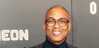 A smiling man in formal attire poses at a red carpet event