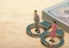 Miniature figures of a man and woman standing on handcuffs next to a stack of money