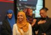 A group of women in cultural attire smiling at an event with a political backdrop