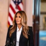 A woman in formal attire speaking at a podium in front of an American flag