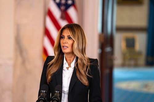 A woman in formal attire speaking at a podium in front of an American flag