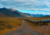 A long pipeline running through a mountainous landscape under a cloudy sky