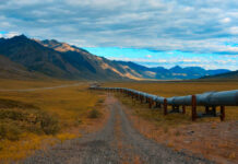 A long pipeline running through a mountainous landscape under a cloudy sky