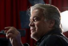 Man with gray hair speaking at an indoor event with dramatic lighting