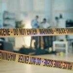 Police crime scene tape blocking an area with investigators in the background