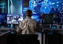 Military personnel monitoring multiple screens in a command center