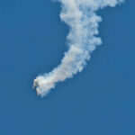 An aircraft performing a stunt with a smoke trail against a blue sky