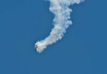 An aircraft performing a stunt with a smoke trail against a blue sky