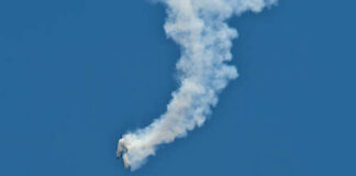 An aircraft performing a stunt with a smoke trail against a blue sky