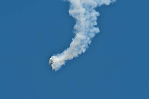 An aircraft performing a stunt with a smoke trail against a blue sky