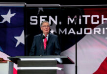 Man speaking at podium with flag background