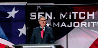 Man speaking at podium with flag background