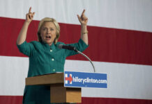 Person speaking emphatically at podium against striped backdrop