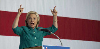 Person speaking emphatically at podium against striped backdrop