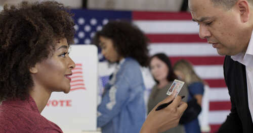 Mixed-race,Staff,Person,Inspects,Photo,Id,,Driving,License,,Presented,By A woman showing her ID to a man at a voting station